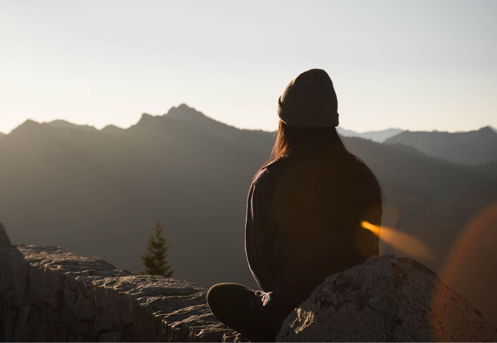 silhouette of a woman sitting on rocks looking out over a mountain with sunrise in the background