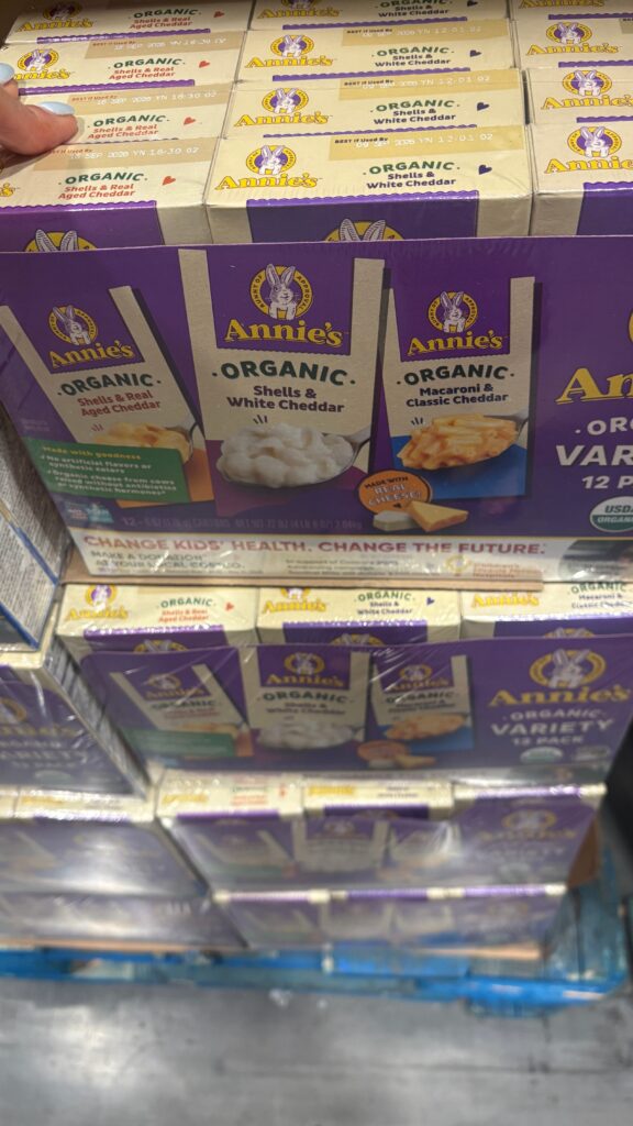 Another view of Annieās Organic Mac and Cheese variety packs on a warehouse display pallet. Boxes are stacked with visible flavor names and USDA Organic labeling.